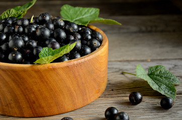 Harvest, ripe black currants, in a wooden bowl on old wooden boards.