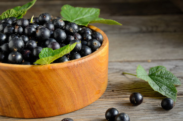 Harvest, ripe black currants, in a wooden bowl on old wooden boards.
