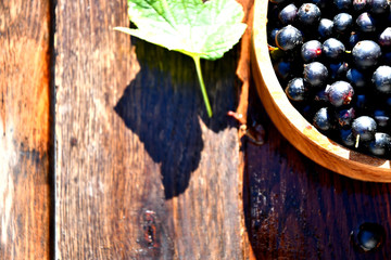 Black currant in a wooden bowl on the background of old boards, top view.