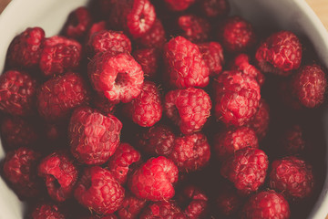 Fresh raspberries background closeup photo. Red raspberries in bowl on wooden table. Vintage style