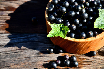 Black currant in a wooden bowl on the background of old boards, top view.