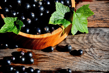 Black currant in a wooden bowl on the background of old boards, top view.