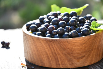 Harvest, ripe black currants, in a wooden bowl, in the garden on a sunny summer day, on old wooden boards.