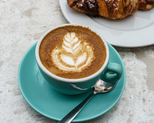 Top view of cup of coffee with foam and croissant on the table.