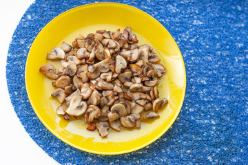 Mushrooms champignons on the yellow plate on the blue table napkin on the white table