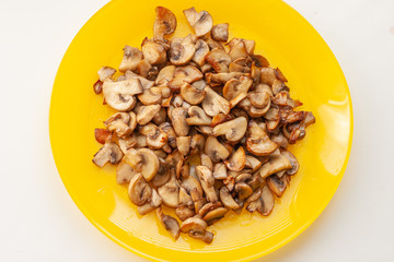 Mushrooms champignons on the yellow plate on the white table