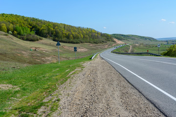 A winding highway stretching into the distance against the backdrop of a beautiful spring landscape, fields, meadows, forests and hills. Road stripes on asphalt.