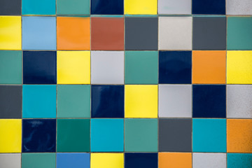 wall of bright multi-colored yellow, blue, white, gray square ceramic tiles. rough surface texture