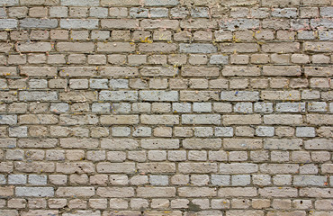 old battered gray brick wall with dark cement and holes in bricks. rough surface texture
