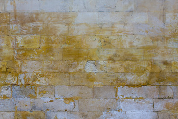 old damaged gray wall of large bricks with bright yellow spots of paint. rough surface texture
