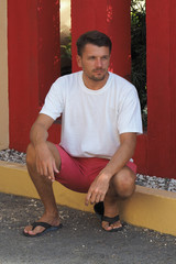 Lifestyle Portrait of a man wearing a white T-shirt coral shorts on the street. red wall...