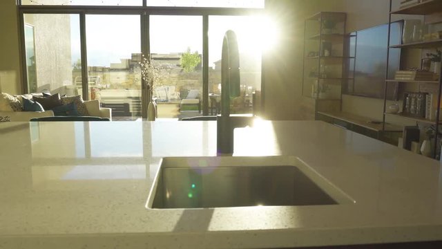 Kitchen Island Faucet with Sun Flare Move Left. view moves left on a detail shot of a kitchen island faucet with a sun flare in the background through window