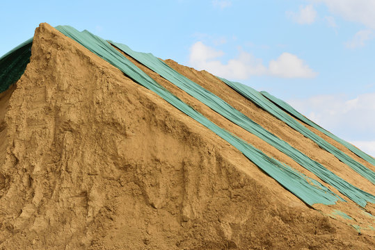 Lehmhaufen mit gr&uuml;nen Planen vor blauem Himmel