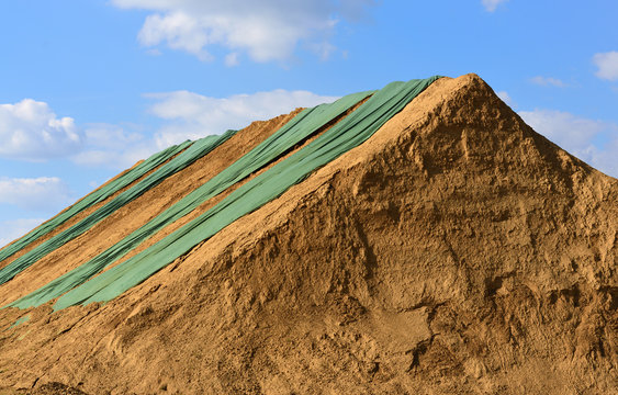 Lehmhaufen mit gr&uuml;nen Planen vor blauem Himmel