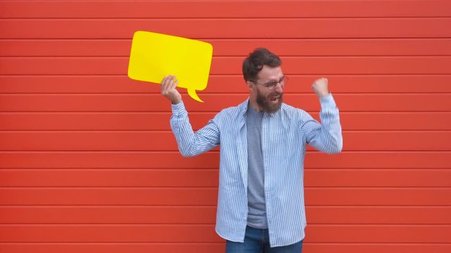Cheerful young man holding a dialog cloud or rectangular yellow bubble speech on red background