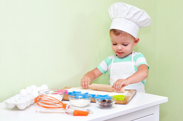 Cheerful cute baby boy in a chef costume standing at the table where rolling dough