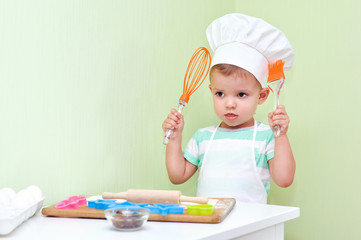 A little cute boy holds an orange whisk for eggs and kitchen silicone brush.