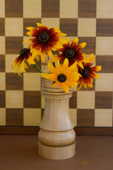 Yellow flowers of perennial rudbeckia in a wooden vase in the shape of a chess rook background of a chessboard