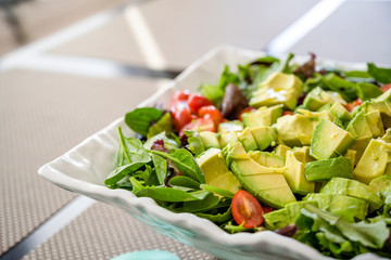 Natural vegetable salad with green leaves and tomato and avocado containing vitamins and fiber in ceramic dish on the table