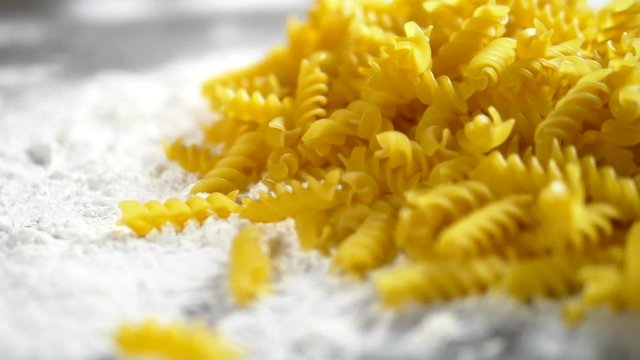 raw pasta fusilli, closeup lie in white flour on a wooden table.