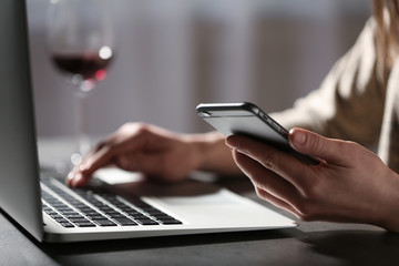 Woman using smartphone and laptop at table indoors, closeup. Loneliness concept