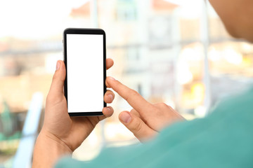 Man holding smartphone with blank screen on blurred background, closeup of hands. Space for text