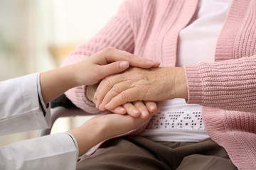 Nurse holding hands of elderly woman against blurred background, closeup. Assisting senior generation