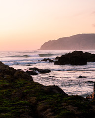 Pink sunset sky, beautiful ocean, sand  and green rocks. Portuese beach. Amazing landscape