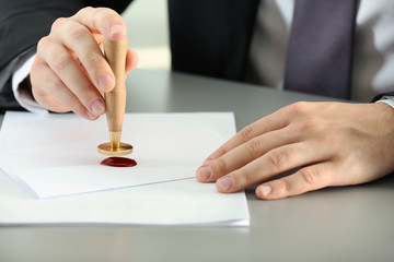 Male notary sealing document at table, closeup