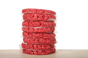 Stack of raw hamburger meat patties on a wood table with pieces of parchment paper between the...