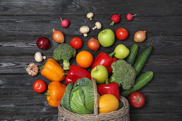 Basket with scattered fruits and vegetables on black wooden table, flat lay