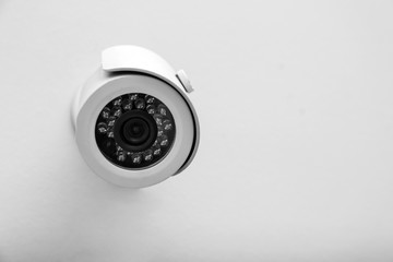 Modern CCTV security camera on white wall. Space for text