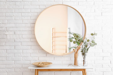 Big round mirror, table with jewelry and decor near brick wall in hallway interior © New Africa