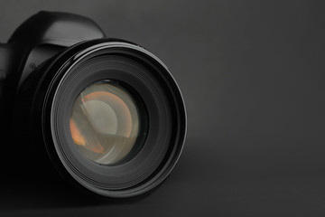 Modern camera with lens on black background, closeup. Space for text