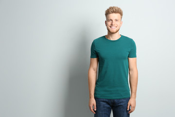 Young man wearing blank t-shirt on light background. Mockup for design