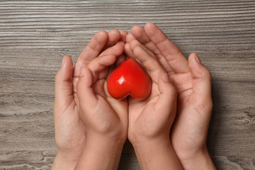Woman and child holding heart on wooden background, top view. Donation concept