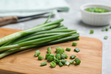Wooden board with bunch of fresh green onion on table, closeup