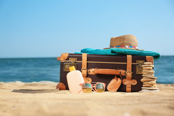 Suitcase and beach accessories on sand near sea. Space for text