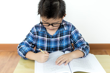 Little student boy in glasses doing his homework on the table with white background