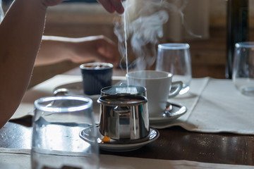 Small metal teapot with tea bag, Some glasses on the restaurant table. White steam rises above hot water..Selective focus