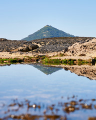 Mountain reflection on the water pond between the rocks at the beach
