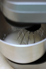 Whipping egg whites in professional kitchen mixer in a restaurant. Close-up whipped whites and sugar in a metal planetary blender bowl.