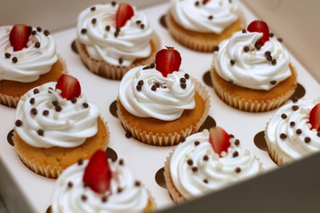 Close-up cupcakes with whipped eggs cream decorated fresh strawberry and chocolate balls in white paper box