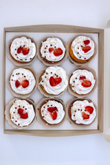 Close-up cupcakes with whipped eggs cream decorated fresh strawberry and chocolate balls in white paper box