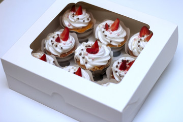 Close-up cupcakes with whipped eggs cream decorated fresh strawberry and chocolate balls in white paper box with transparent cover