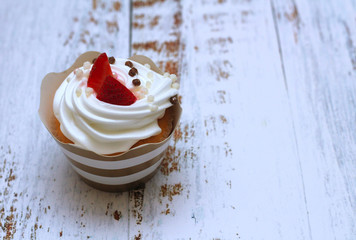 Close-up cupcake with whipped eggs cream decorated fresh strawberry and chocolate balls on old white wooden table background.