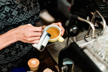 Close up of barista hand pouring stremed milk into white cup of coffee to create latte art.