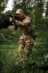 Fototapeta premium Airsoft soldier in full ammunition with rifle playing strikeball in outdoor in grass