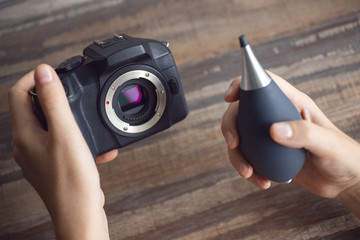 Two hands cleaning digital camera sensor from dust with air blower