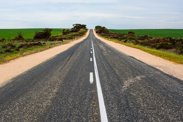 Empty straight asphalt road going through rural Australian countryside with green farmland on either side, South Australia